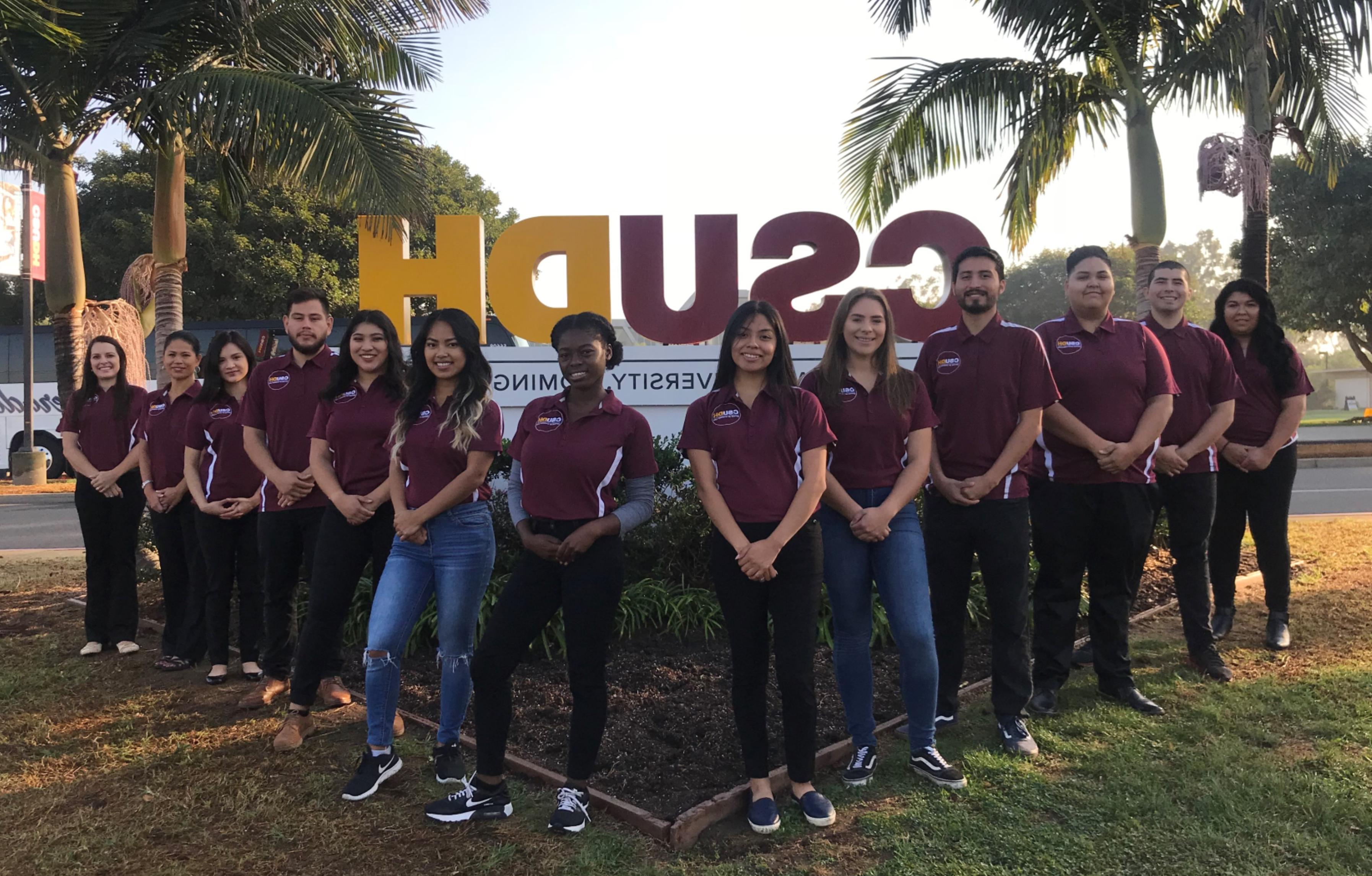 A picture of all staff members who work in the Office of Student Life standing in front of the large CSUDH sign on Victoria Street.